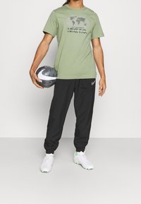 Camiseta de algodón verde con un gráfico del mundo y el texto "NIKE", combinada con pantalones jogger negros y zapatos deportivos blancos con acentos verdes.