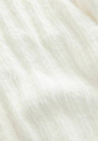 Tissu blanc et duveteux avec une surface texturée, présentant des fibres douces et longues ainsi qu'un éclat subtil, disposées en motifs ondulés.