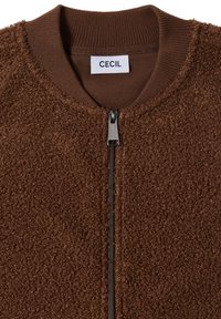 Hnědá fleecová bunda s žebrovaným límcem a manžetami, která má centrální zip a štítek s označením "CECIL". Měkká, strukturovaná látka.