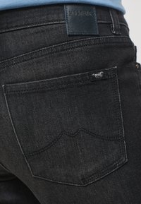 Mörka jeans i denim med en slät textur, utrustade med en läderetikett vid midjan och en bakficka med en broderad emblem och böjda sömmar.