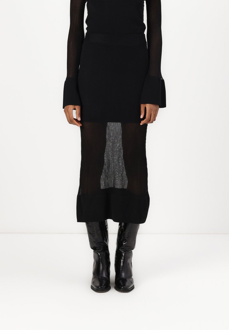 Jupe en maille côtelée noire avec un panneau rayé transparent, dotée d'une taille ajustée et d'un ourlet volanté. Associée à des bottes noires vernies montantes.