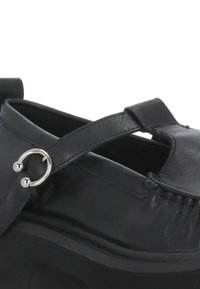 Scarpa in pelle nera con punta arrotondata, fascetta incrociata, dettagli in metallo argentato e suola piatta spessa con grip testurizzati.