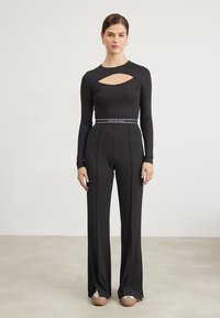 Maglietta nera a maniche lunghe con scollo a cuore, abbinata a pantaloni neri a vita alta e gamba larga con cintura a righe.