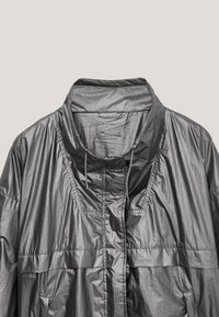 Graue hochkragige leichte Jacke mit Kordelzug, vorderen Klappentaschen und strukturiertem Stoff, auf einem neutralen Hintergrund präsentiert.