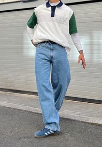 Vit och grön färgblockerad pikétröja med marinblå krage, i kombination med ljusblå vida jeans och blå sneakers med tre ränder.