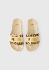 Puma-liukusandaalit, joissa on beige pohja, eläinkuosilla varustettu remmi ja kultainen logovaihtoehto. Teksturoitu materiaali mukavuutta ja pitoa varten.