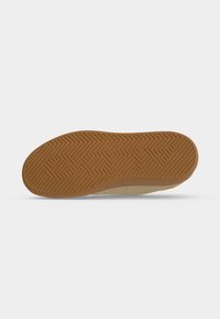 Semelle d'une basket beige avec une semelle extérieure en caoutchouc marron présentant des rainures diagonales et le mot "AMAZON" embossé.