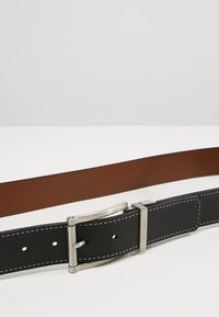 Cintura reversibile in pelle nera e marrone con fibbia in metallo argento, caratterizzata da cuciture bianche e una texture distinta su entrambi i lati.