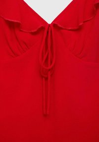 Haut rouge avec un col en V orné de volants, tissu froncé autour du décolleté, et fermeture à cordon au dos.