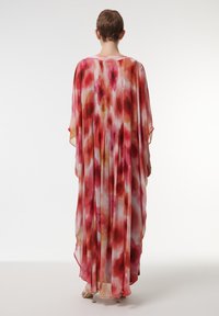 Vloeiende, geplooide kaftan van doorschijnende stof met een aquarelpatroon van rode, roze en oranje tinten. Wijde mouwen en een ronde halslijn.