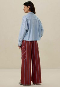 Helleblaue, verkürzte Jeansjacke kombiniert mit weiten roten Hosen, die vertikale blaue Streifen und seitliche Cargo-Taschen haben.