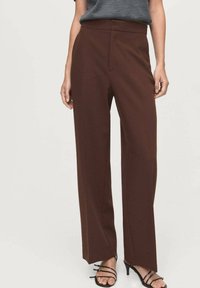 Pantalones marrones de pierna ancha en una tela suave, con un ajuste a medida, pliegue frontal y bolsillos laterales. Emparejados con tacones negros con tiras.