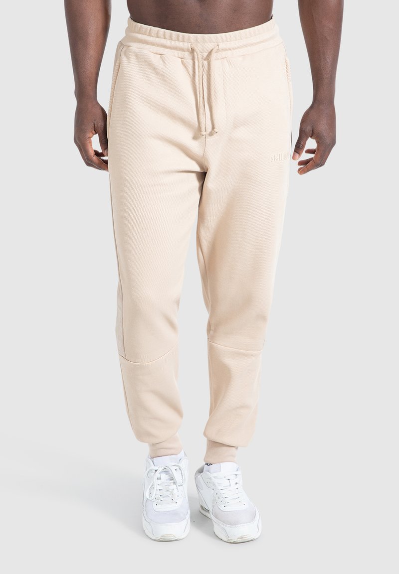 Beige sweatpants met een gestructureerde afwerking, elastische tailleband en verstelbare trekkoorden. Heeft taps toelopende pijpen en naadloze knie details.
