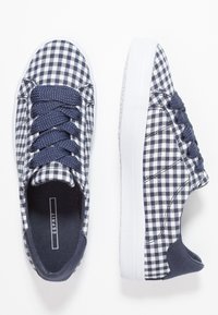Granatowo-białe tenisówki z płótna w kratę, z zaokrąglonym noskiem, białą podeszwą i sznurowadłami z teksturowanego materiału. Charakteryzują się przeszyciami na bokach.