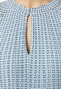 Lichtblauw blouse met een bloemenpatroon, voorzien van een keyhole-nek en subtiele plooien. Gemaakt van zachte stof, met een lichtgewicht textuur.