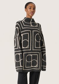 Oversized sort striktrøje med cremefarvede geometriske mønstre, høj krave og lange ærmer. Blød tekstur; afslappet pasform.