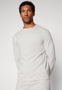 Camiseta de manga larga gris claro con cuello redondo y corte relajado. Textura suave, detalles de costura sutiles y dobladillo recto.