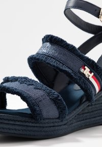 Sandalo wedge navy con fasce in tessuto testurizzato, bordo con frange e un accento argentato con il logo del marchio; piattaforma intrecciata per stabilità.
