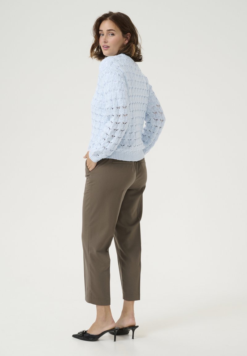 Hellblauer Strickpullover mit strukturiertem Muster, gerippten Bündchen und Saum, kombiniert mit braunen schmal geschnittenen Hosen und schwarzen High Heels.