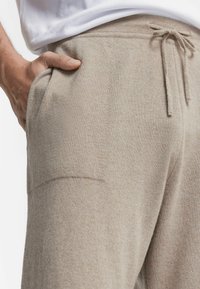 Beżowe dresowe spodnie z gładką teksturą, elastycznym pasem i sznurkiem do regulacji. Posiadają boczne kieszenie oraz subtelne detale szwów.