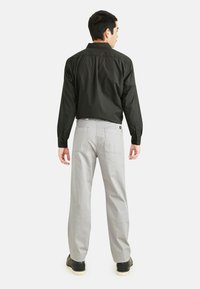 Chemise noire à manches longues avec poignets à boutons, associée à un pantalon droit gris avec poches arrière et une étiquette de logo.