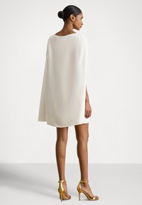 Balta apsiausto stiliaus suknelė su apvalia iškirpte, lengvai krentančia medžiaga ir šoninėmis anga, derinama su auksinėmis aukštakulnėmis sandalais. Lygi tekstūra.