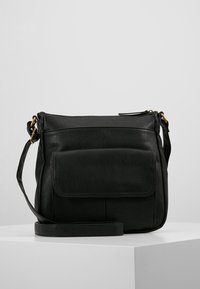 Svart läder crossbody-väska med framficka, justerbar rem och guldfärgad hårdvara på en vit yta med ljusgrå bakgrund.