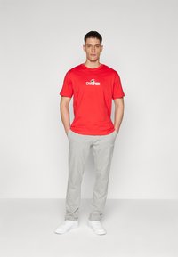 Rød kortærmet t-shirt med "Champion" logo på brystet, parret med lysegrå sweatpants. Hvite sneakers fuldender det afslappede outfit.