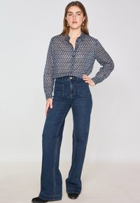 Blusa a fantasia marina con design a colletto, abbinata a jeans scuri a vita alta. Tessuto liscio con maniche lunghe e bottoni discreti.