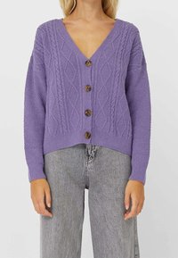 Paars gebreid cardigan met een V-hals, met een gestructureerd kabelpatroon en vijf bruine knopen aan de voorkant. Ontspannen pasvorm en ribgebreide onderkant.