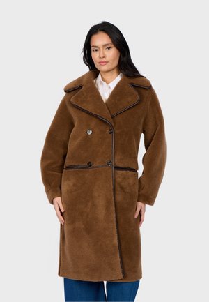 Manteau en fausse fourrure marron avec un large col, des boutons double boutonnage, et des accents sombres contrastants le long des coutures. Manches longues et longueur aux genoux.