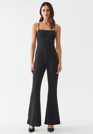 Mono negro con tirantes finos, cuerpo ajustado, piernas acampanadas y textura suave. Diseño sencillo sin patrones ni adornos.