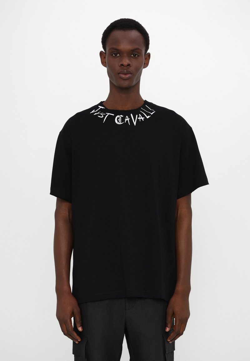 Black cotton t-shirt with a relaxed fit, featuring white text "Just Cavalli" printed around the crew neckline. Short sleeves and simple design.
