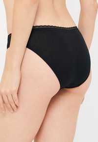 Mutande in tessuto nero caratterizzate da una texture liscia e da un bordo in pizzo in vita. Il design offre una copertura completa con una forma classica.
