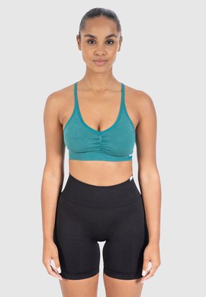 Teal geribbelde sportbeha met een diepe V-hals en een geplooid middenstuk. Hoge zwarte shorts met een soepele tailleband, beide van rekbaar materiaal.