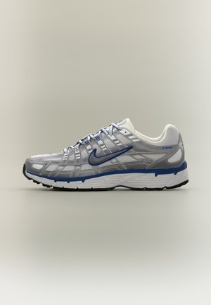 Witte en zilveren Nike hardloopschoen met blauwe accenten, blauw swoosh-logo en zwarte rubberen zool, van opzij getoond op een neutrale achtergrond.