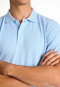 Polo azzurro chiaro realizzato in misto cotone, con colletto a coste, pattina con due bottoni e piccolo logo ricamato sul lato sinistro del petto.