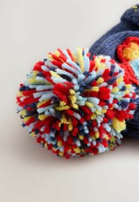 Accessoire en pompon tricoté en matériau bleu avec des brins rouge vif, jaune et bleu clair. Présente une texture douce et multicolore.