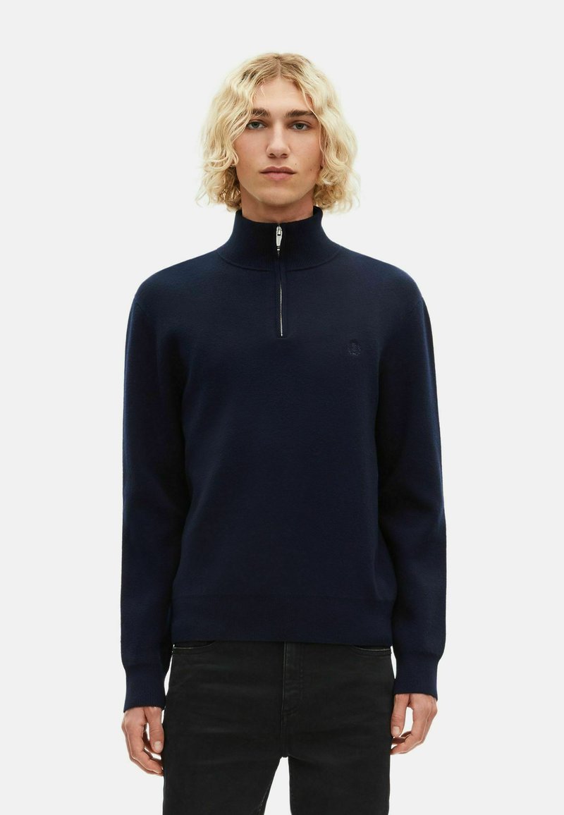 Granatowy półzapinany sweter wykonany z miękkiego materiału, z prążkowanym kołnierzem i mankietami, z subtelnym logo po lewej stronie klatki piersiowej.