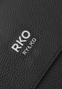 Pelle nera texturizzata con logo argentato in rilievo "RKO RYŁKO," caratterizzata da una finitura a ciottoli e un design minimalista.