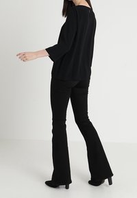 Haut noir fluide à manches trois-quarts, associé à un pantalon noir évasé ajusté. Les deux pièces présentent des textures douces et une silhouette épurée.
