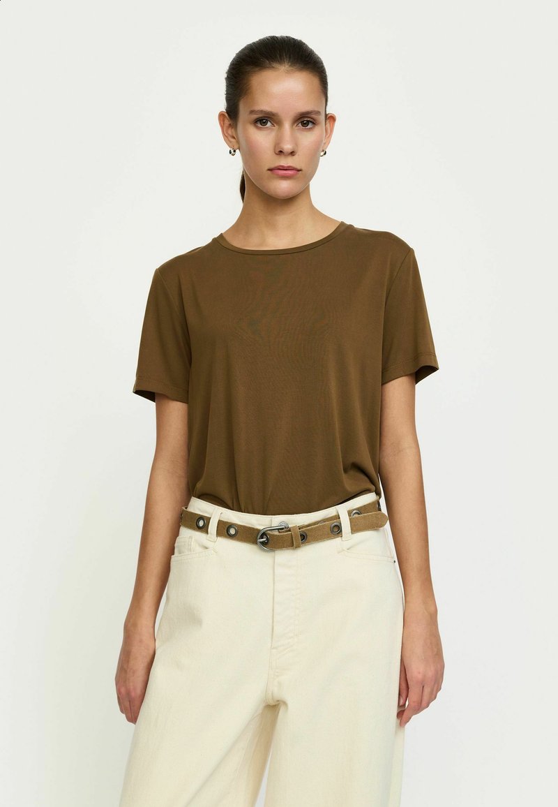 T-shirt marron à manches courtes en tissu lisse, assorti à un pantalon de couleur crème et une ceinture camel avec des accents métalliques.
