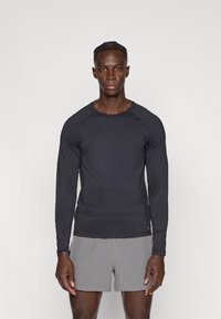 Μακρυμάνικη αθλητική μαύρη μπλούζα σε εφαρμοστή γραμμή, κατασκευασμένη από λείο ύφασμα, συνδυασμένη με ανοιχτό γκρι σορτς. Απλή και λειτουργική εμφάνιση.