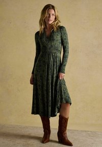 Długo rękawowa, zielona sukienka w kwiaty z dopasowanym gorsetem i rozkloszowaną spódnicą. Zestawiona z brązowymi kowbojkami na obcasie z ozdobnym haftem.