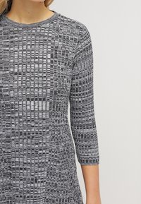 Robe en tricot grise et noire à motif, avec des manches trois-quarts, un col rond et un design texturé présentant des détails en forme de grille.