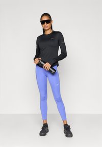 Μαύρο αθλητικό μπλουζάκι με μακριά μανίκια και μικρό λογότυπο, σε συνδυασμό με ανοιχτό μοβ κολάν. Μαύρο παγούρι και παπούτσια ολοκληρώνουν την εμφάνιση.