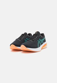 Chaussures de sport noires avec des accents verts et une tige texturée. Semelles extérieures orange, design à lacets et construction de soutien pour le confort.