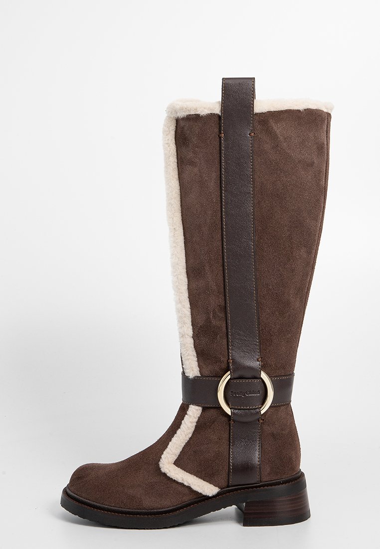 Bruine suède kniehoge laars met witte nepbont voering, bruine leren band en gouden ringdetails. Gevoerde zool en licht uitlopende hak.