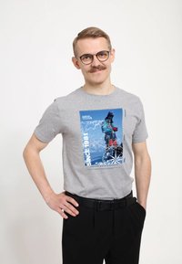 Szara bawełniana koszulka z graficznym nadrukiem przedstawiającym górski krajobraz z wspinaczem, z niebieskimi akcentami i napisem "SINCE 1981".