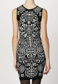 Abito bodycon bianco e nero con intricati motivi floreali, design senza maniche, scollatura rotonda e dettagli in tessuto testurizzato.